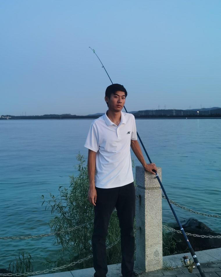 Anthony standing at a lakeside railing at dusk, holding a fishing rod.